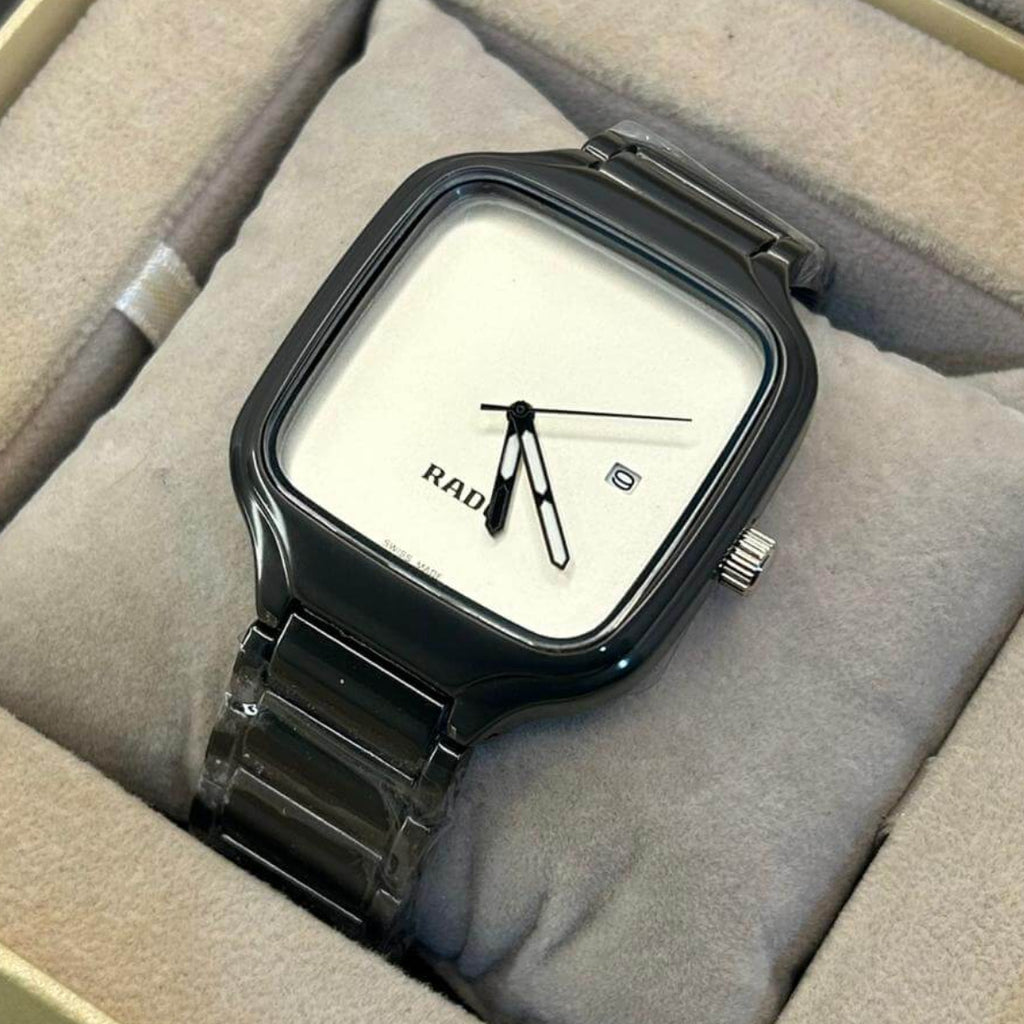 A Rado analog watch with a square black case, white dial, and black metal link bracelet, presented inside a beige cushioned watch box.