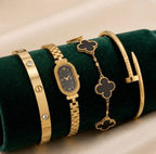 A gold-tone jewelry set featuring a watch, bracelet, and bangles displayed on a dark green velvet cylindrical stand against a beige satin background.