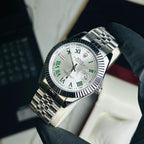 A Rolex Submariner Date watch with a silver-tone metal bracelet and a white dial featuring green Roman numerals, held by a hand wearing a black glove.